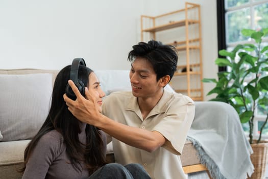 Young couple relax together and boyfriend put headphone on girlfriend. Romantic day together. Valentine's Day concept.