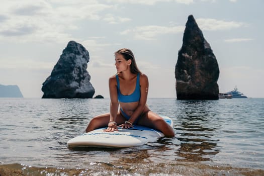 Close up shot of beautiful young caucasian woman with black hair and freckles looking at camera and smiling. Cute woman portrait in a pink bikini posing on a volcanic rock high above the sea