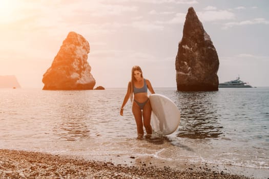 Close up shot of beautiful young caucasian woman with black hair and freckles looking at camera and smiling. Cute woman portrait in a pink bikini posing on a volcanic rock high above the sea