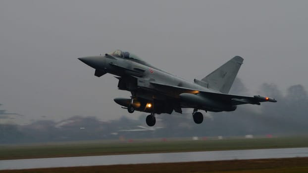 Istrana Italy December 13 2023: Combat aircraft lifts off a flooded runway, casting massive water clouds. Includes copy space. NATO air defense capability in all weather. Copy Space.