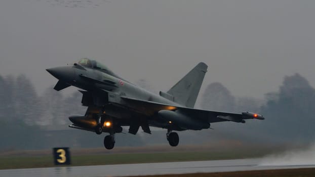 Istrana Italy December 13 2023: Combat aircraft lifts off a flooded runway, casting massive water clouds. Includes copy space. NATO air defense capability in all weather. Copy Space.
