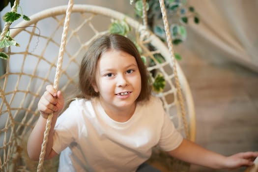A little girl is relaxing in a room with a wicker chair. A schoolgirl is lazy after school. Teen idling at home