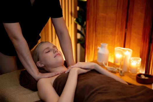 Caucasian woman customer enjoying relaxing anti-stress spa massage and pampering with beauty skin recreation leisure in warm candle lighting ambient salon spa at luxury resort or hotel. Quiescent