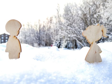 Wooden toys of boy and girl on white snow. Couple in love on Valentine's Day in February. Love in cold world and forest background