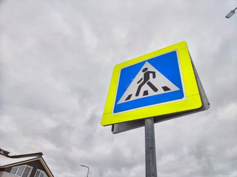 A pedestrian crossing sign on the background of a gray sky with clouds. Drawing, pictogram for pedestrians crossing the road