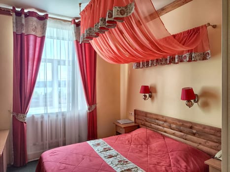 Small compact stylish bedroom in stylish soothing With double bed with red bedspread and a canopy. Concept of small cozy bedroom or hotel room