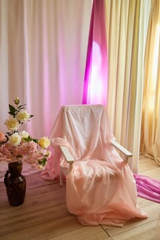 Delicate pink bright interior of the room with an armchair, vase with roses, draped curtains and a window. Location and background in the photo studio