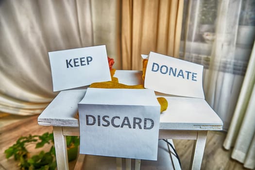 Signs with the words keep, donate, discard and fashion clothes folded in stacks in cozy room. The concept of cluttering and decluttering. Background