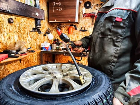 Ishim, Russia - November 27, 2023: Mechanic repairs a car wheel and makes a tire in a dirty garage. Replacement of summer wheels, tires for winter indoors