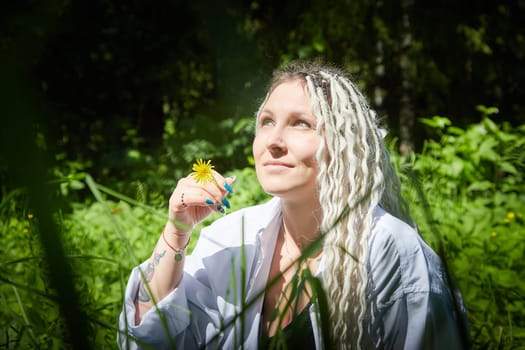 Kirov, Russia - June 12, 2023: Hippy girl enjoys life in forest on a sunny spring or summer day. Woman in green nature landscape
