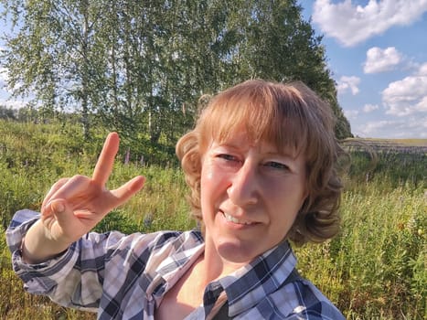 Happy female blonde tourist taking selfie picture with smart mobile phone outside. Middle aged woman having fun on adventure nature trip on nature