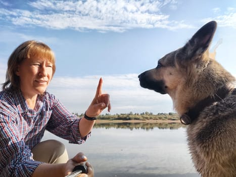 Adult girl with shepherd dog taking selfie in forest. Middle aged woman and big shepherd dog on nature. Friendship, love, fun, hugs