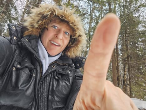 Happy, cheerful middle-aged woman in a warm jacket and a hood with fur taking selfie in winter outdoors. Female Traveler in Alaska, Lapland, Arctic, Siberia