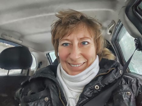 Funny shaggy-haired girl or a middle-aged woman drives a car in winter, autumn, and spring in the cold. A female driver on a solo trip
