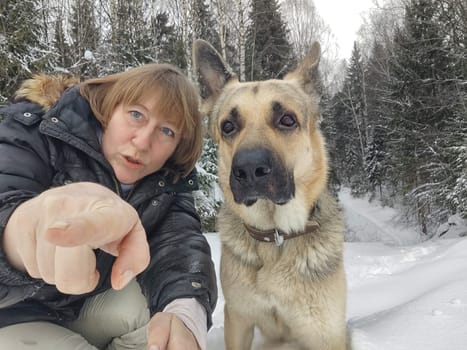 Adult girl with shepherd dog taking selfies in winter forest. Middle aged woman and big shepherd dog on nature in cold day. Friendship, love, communication, fun, hugs