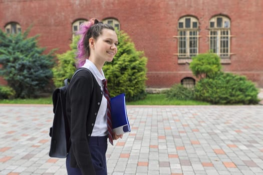 Outdoor portrait of schoolgirl near school building, beautiful trendy teenager girl with backpack going school, copy space