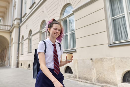 Girl student 15, 16 years old walking with backpack cup of drink. Back to school, college