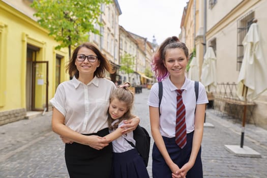 Happy mother and daughters going to school. Woman hugged youngest girl, positive smiling family. Back to school