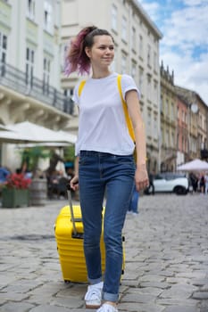 Traveler girl walking with backpack and yellow suitcase along the street of tourist city