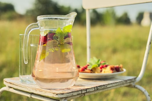 Hello summer, strawberry season. Cake with berries and jug with strawberry mint drink on vintage chair in summer sunny meadow, background nature grass