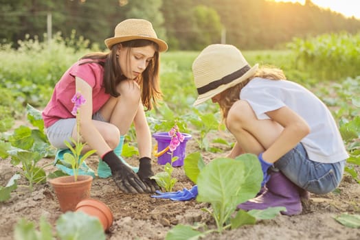 Children two beautiful girls in hats with flowers in pots, gloves with garden tools, planting plants in ground. Background spring summer landscape, nature, sky