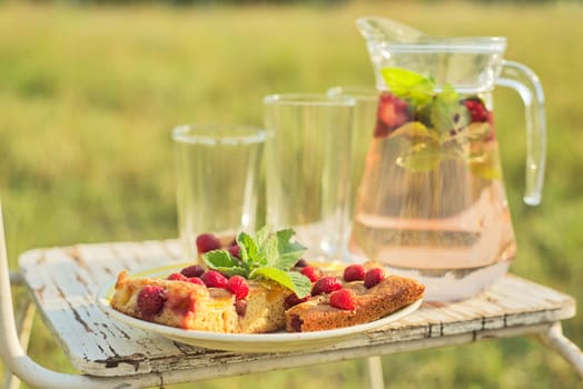 Hello summer, strawberry season. Cake with berries and jug with strawberry mint drink on vintage chair in summer sunny meadow, background nature grass
