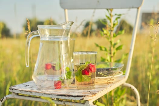 Summer natural vitamin berry drinks, jug and glasses with drink strawberry mint, plate with mulberry, background of summer herbs flowers on lawn, sunny day