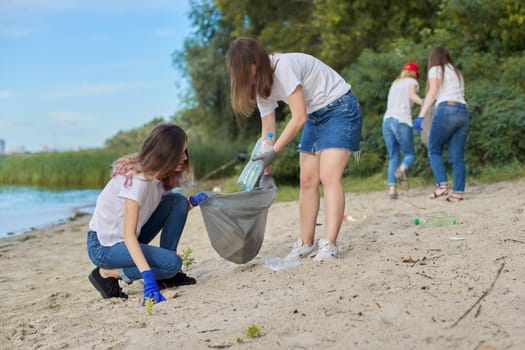 Group of teenagers on riverbank picking up plastic trash in bags. Environmental protection, youth, volunteering, charity, and ecology concept