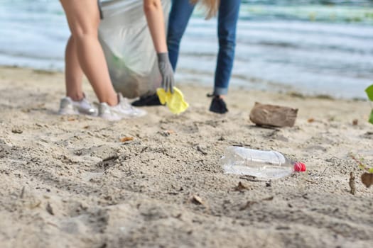 Group of teenagers on riverbank picking up plastic trash in bags. Environmental protection, youth, volunteering, charity, and ecology concept