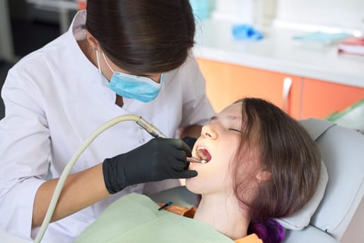 Woman dentist treating teeth to a patient sitting in dental chair using professional equipment. Dentistry, healthy teeth, sedation, medicine and healthcare concept