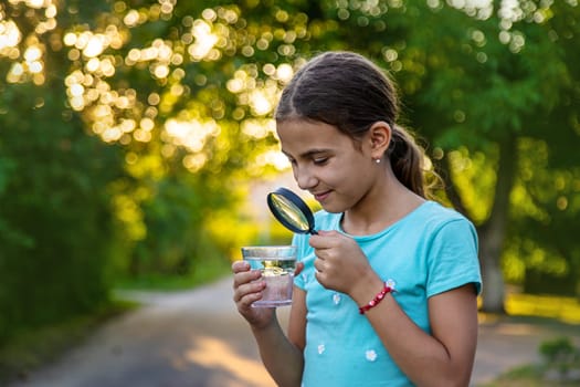 A child looks into a glass of water with a magnifying glass. Selective focus. Drink.