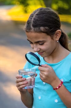 A child looks into a glass of water with a magnifying glass. Selective focus. Drink.