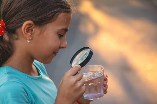 A child looks into a glass of water with a magnifying glass. Selective focus. Drink.