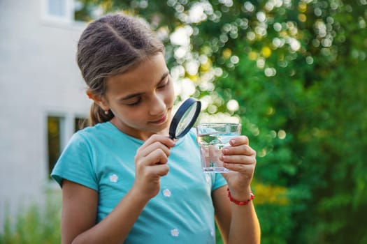 A child looks into a glass of water with a magnifying glass. Selective focus. Drink.