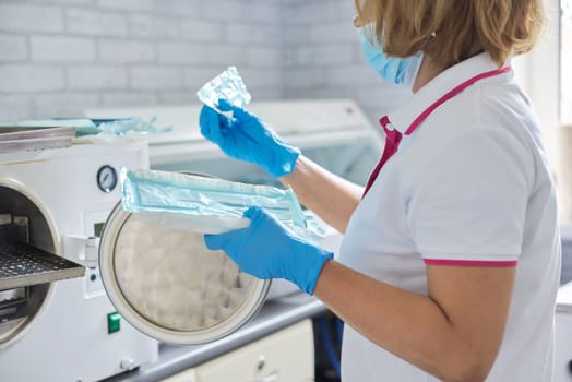 Female nurse doing sterilization of dental medical instruments in autoclave. Sterilization department at dental clinic