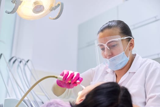 Woman dentist treating teeth to a patient sitting in dental chair using professional equipment. Dentistry, healthy teeth, sedation, medicine and healthcare concept