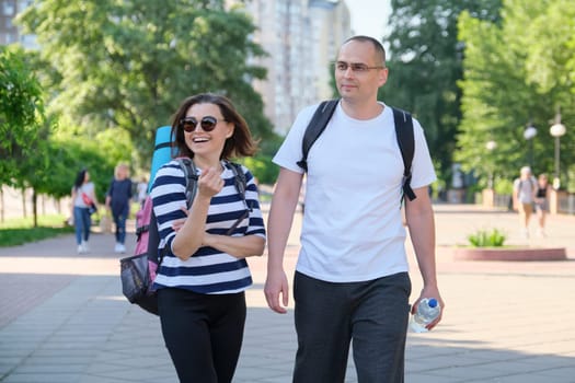 Outdoor walking man and woman, talking people, middle-aged couple in sportswear with backpacks, active healthy lifestyle and relationships of age 40 years old people