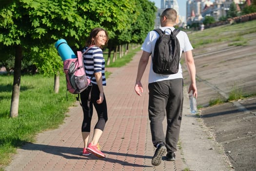 Talking middle-aged man and woman, couple walking along park road for sports fitness training, active healthy lifestyle and relationships of age 40 years old people