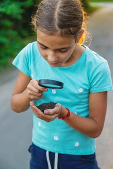 The child looks at the soil in his hands with a magnifying glass. Selective focus. Kid,