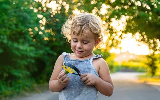 A child looks at a flower with a magnifying glass. Selective focus. Kid.