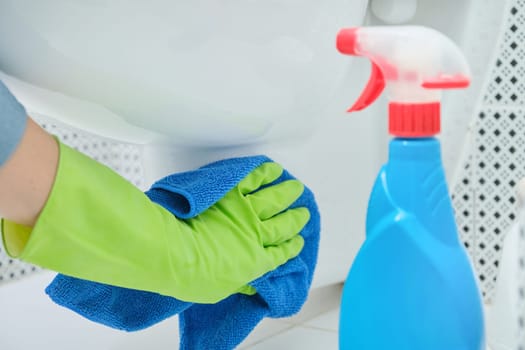 Close-up of woman hand in gloves with rag and detergent washing hanging toilet, home cleaning in bathroom