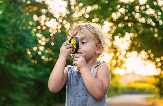 A child looks at a flower with a magnifying glass. Selective focus. Kid.