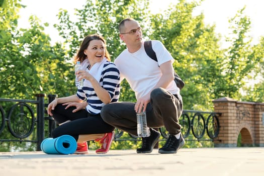 Happy smiling mature couple sitting in the park, talking man and woman resting after doing sports. Communication and relationship age people, active lifestyle