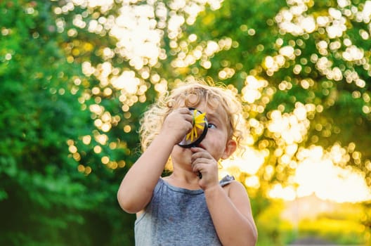 A child looks at a flower with a magnifying glass. Selective focus. Kid.