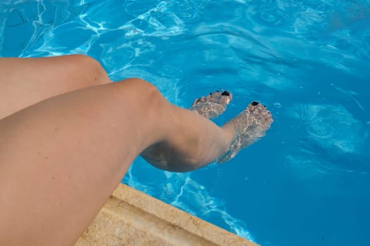 Woman legs in outdoor pool, sunny summer day, rest in resort spa hotel