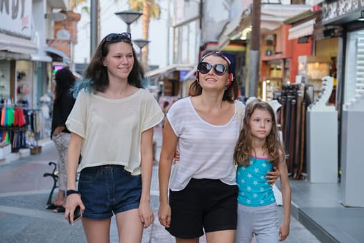 People mother and two daughters walking along street of small resort town, family vacations together, summer fun shopping in souvenir shops