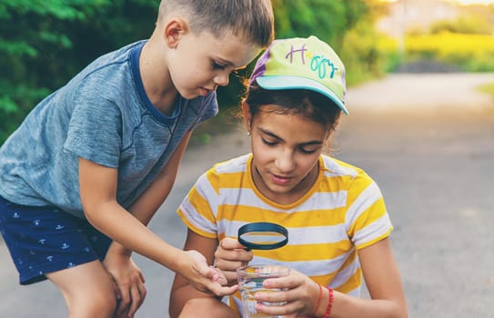 Children look with a magnifying glass into a glass of water. Selective focus. Kid.