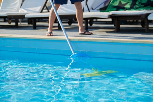 Male cleaning outdoor swimming pool with underwater vacuum tube.