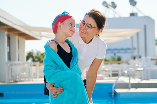 Active healthy lifestyle, mother and daughter child in sport hat goggles for swimming with towel near the outdoor pool