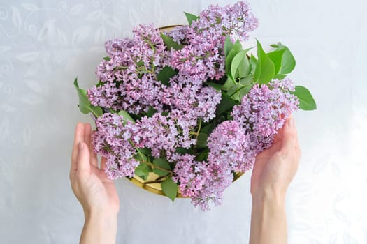 Woman florist with lilac floral decoration. Light background, female holding golden tray with flowers in her hands for interior decoration
